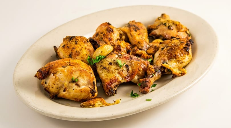 Platter of golden-brown roasted chicken pieces with garlic cloves and parsley garnish.