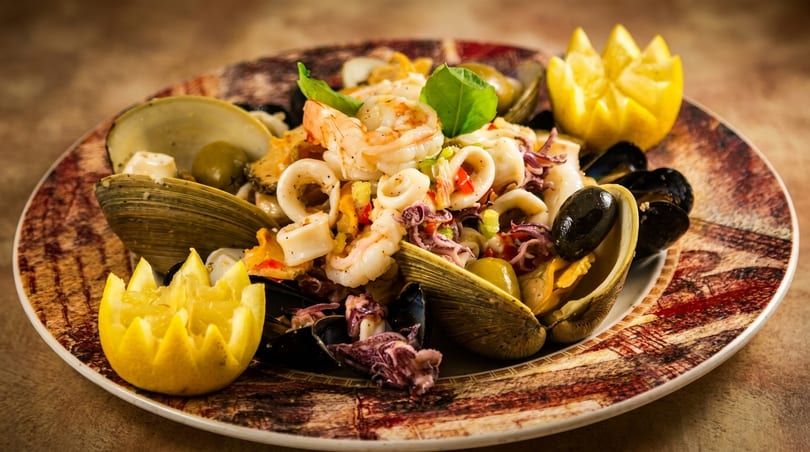 Seafood salad with shrimp, calamari, mussels, clams, olives, and lemon wedges on a decorative plate.