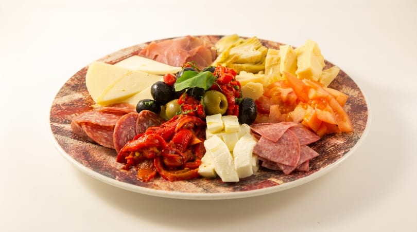 A colorful antipasto platter with various cheeses, meats, olives, sun-dried tomatoes, and artichoke hearts.