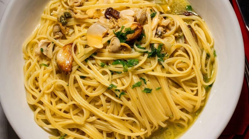 Close-up of linguine pasta with clams, garlic, and parsley in a white bowl.