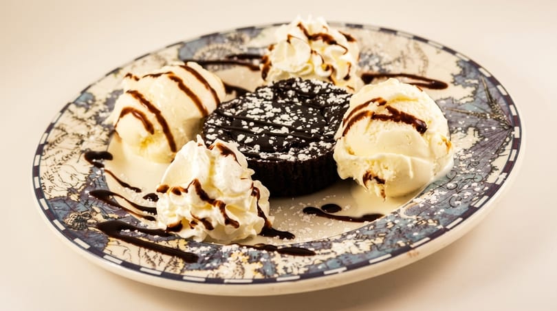 Chocolate lava cake with powdered sugar, vanilla ice cream, whipped cream, and chocolate syrup on a plate.